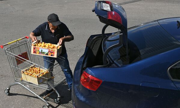 Мужчина загружает ящики с абрикосами в машину на территории торгового комплекса Бухта в Москве - Sputnik Армения