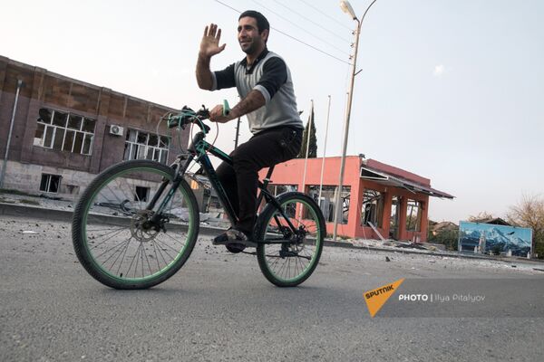 Житель Мартакерта проезжает на велосипеде мимо разрушенных вследствие обстрелов зданий (30 октября 2020). Карабах - Sputnik Армения