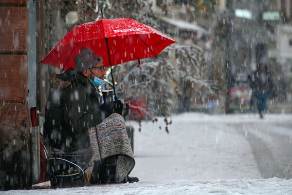 Бездомный мужчина сидит на тротуаре во время снегопада в городе Мюлуз в восточной Франции - Sputnik Армения