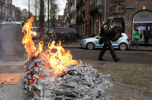 Полицейский проходит мимо зажженного на улице костра во время акции протеста против ограничений в связи с коронавирусом (24 января 2021). Амстердам - Sputnik Армения