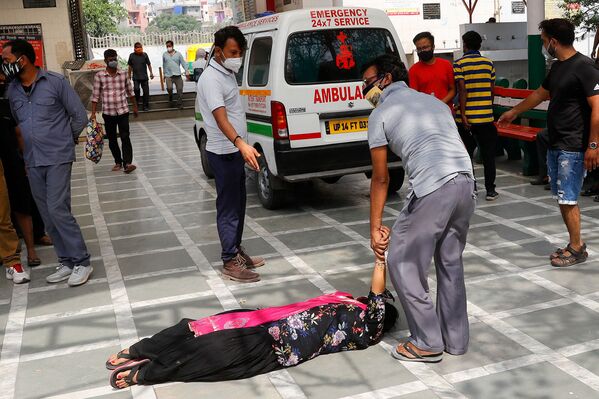 Мужчина пытается поднять женщину, упавшую в обморок после того, как увидела тело родственника в крематории Нью-Дели, Индия - Sputnik Армения