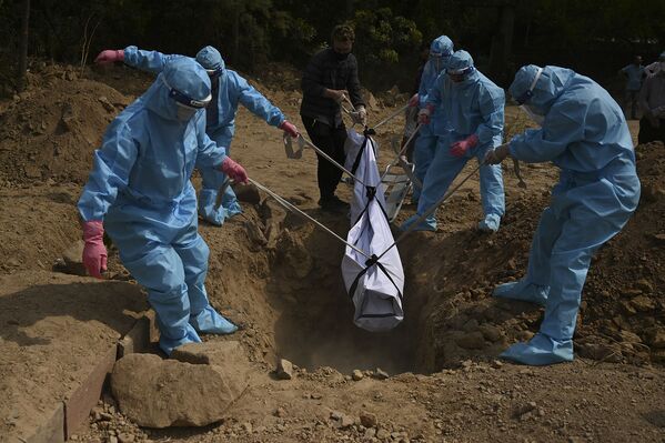 Люди в защитных костюмах опускают тело умершего родственника в могилу на кладбище в Нью-Дели, Индия - Sputnik Армения