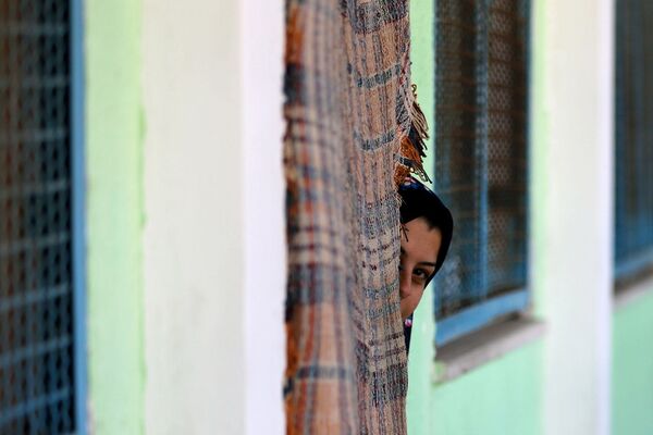 Палестинская женщина, бежавшая из дома из-за израильских ударов, смотрит из класса в школе, принимающей беженцев (15 мая 2021). Газа - Sputnik Армения