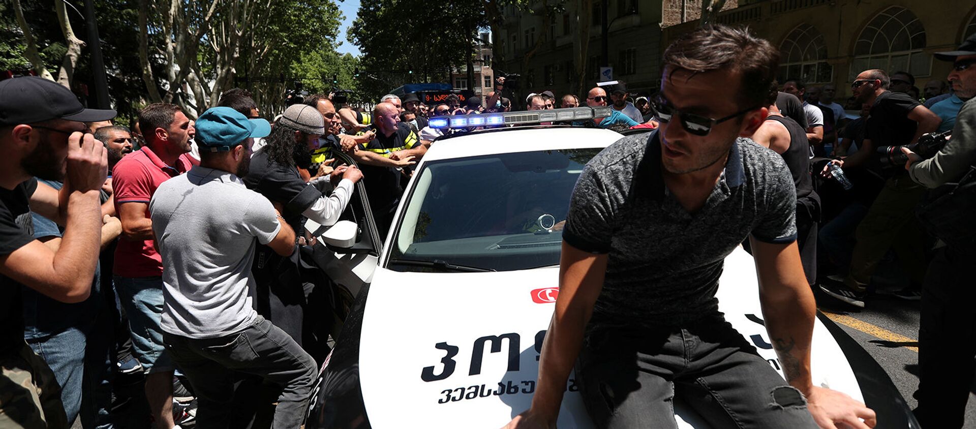 Протестующие пытаются заблокировать полицейскую машину во время митинга перед запланированным Маршем достоинства (5 июля 2021). Тбилиси - Sputnik Армения, 1920, 05.07.2021