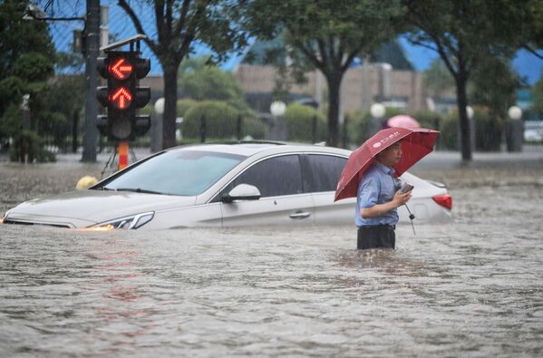 Мужчина у затопленной в результате проливных дождей машины после проливных дождей в Чжэнчжоу в центральной провинции Китая Хэнань - Sputnik Армения