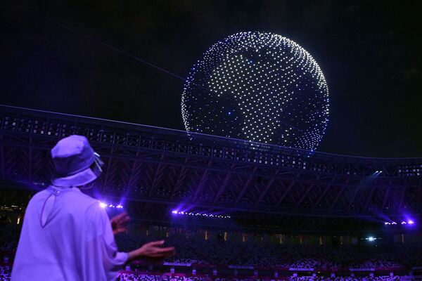 Спортсмены и волонтеры смотрят на глобус из дронов в небе над Олимпийским стадионом во время церемонии открытия Олимпийских игр (23 июля 2021). Токио - Sputnik Армения