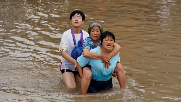 Женщина несет пожилую женщину  через паводковые воды после проливного дождя в Чжэнчжоу, провинция Хэнань, Китай - Sputnik Армения