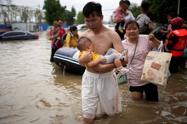 Мужчина с младенцем пробирается по затопленной дороге после проливного дождя в Чжэнчжоу, провинция Хэнань, Китай - Sputnik Армения