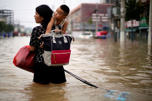 Женщина с ребенком и вещами пробирается через паводковые воды после проливного дождя в Чжэнчжоу, провинция Хэнань, Китай - Sputnik Армения