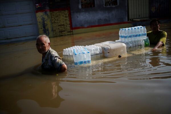 Жители деревни с бутылками с водой пробираются через паводковые воды после проливных дождей в деревне в Синьсяне, провинция Хэнань, Китай - Sputnik Армения
