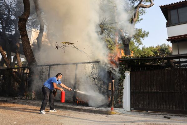Мужчина с огнетушителем пытается тушить лесной пожар в пригороде Варимпомпи к северу от Афин, Греция - Sputnik Армения