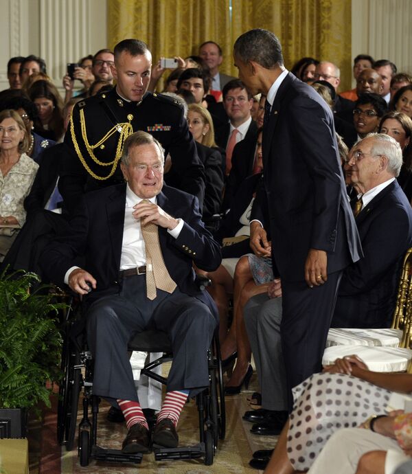 Экс-президент Джордж Буш в красно-белых носках сидит рядом с президентом Бараком Обамой во время вручения 5000-й награды Daily Point of Light Award в Восточном зале Белого дома (15 июля 2013). Вашингтон - Sputnik Армения