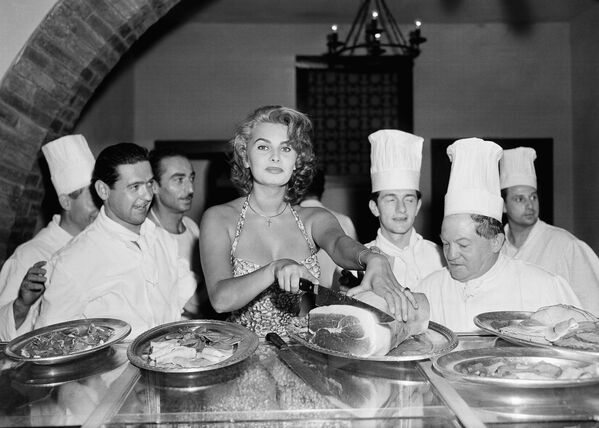 Софи Лорен – прекрасная хозяйка и автор книги рецептов. На этом фото она выскользнула с большой вечеринки в отеле Эксельсиор в Венеции 25 августа 1955 года, чтобы нарезать ветчину на тонкие пластинки. Ее поклонники-повара в восторге. - Sputnik Армения