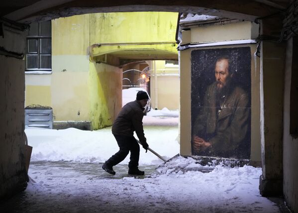 Муниципальный служащий убирает снег во дворе рядом с портретом русского писателя Федора Достоевского, нарисованном на стене недалеко от музея-квартиры Достоевского в центре Санкт-Петербурга - Sputnik Армения