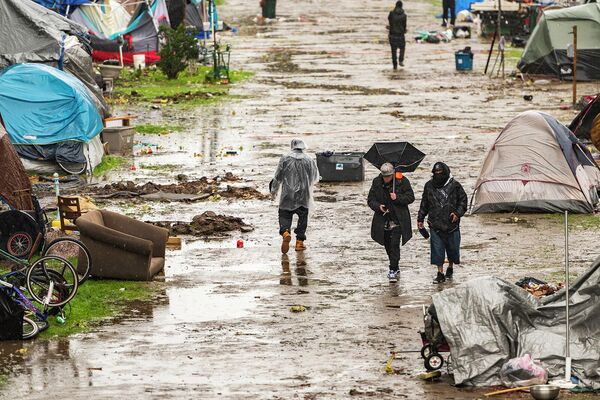 Люди проходят через частично затопленный лагерь для бездомных в парке Риверуолк в Санта-Крус, Калифорния  - Sputnik Армения