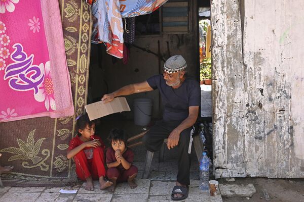 Пожилой житель Газы обдувает куском картона своих детей во время резкого потепленияПалестина, 18 июля 2023 года - Sputnik Армения