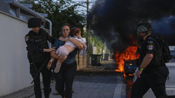 Полицейские эвакуируют женщину и ребенка с места попадания ракеты, выпущенной из сектора Газа (7 октября 2023). Ашкелон - Sputnik Армения