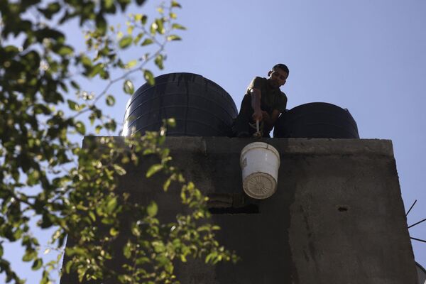 Мужчина поднимает ведро с водой на крышу, чтобы наполнить резервуар для воды в доме в лагере беженцев в Рафахе, на юге сектора Газа. - Sputnik Армения