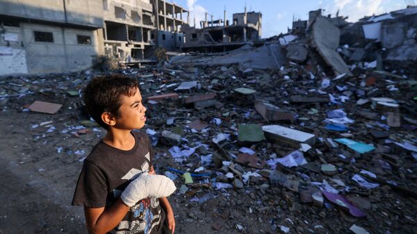 Раненый палестинский мальчик смотрит на здания, разрушенные во время израильских авиаударов, недалеко от его дома в лагере беженцев Рафах на юге сектора Газа - Sputnik Армения