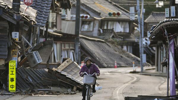 Женщина едет на велосипеде среди поврежденных домов в городе Ното (2 января 2024). Япония - Sputnik Армения