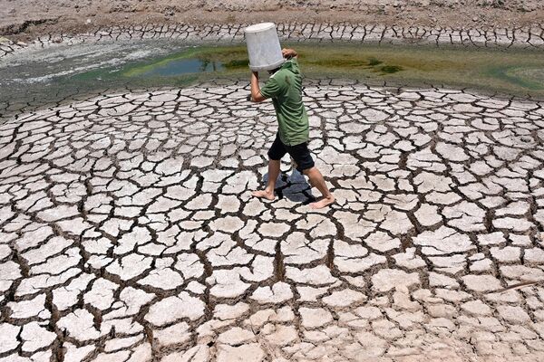 Мужчина несет пластиковое ведро по потрескавшемуся руслу высохшего пруда в Бенче, Вьетнам. - Sputnik Армения