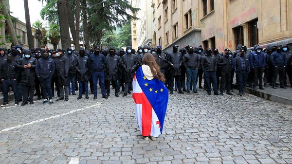 Демонстрант с задрапированными национальными флагами Грузии и ЕС стоит во время акции протеста оппозиции против российского закона  (14 мая 2024). Тбилиси - Sputnik Армения