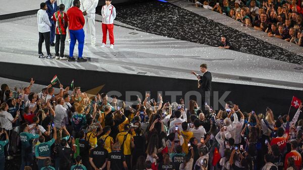 Леон Маршан с олимпийском огнем подходит к президенту МОК Томасу Баху и 6 атлетам во время церемонии закрытия Олимпиады (11 августа 2024). Париж - Sputnik Армения