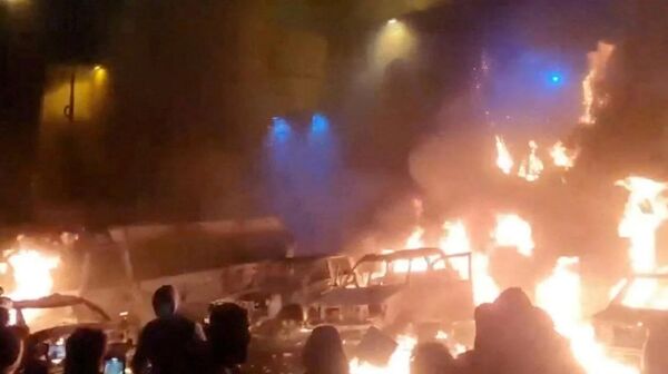 Протестующие на фоне горящих автомобилей во время антиправительственных митингов в Иране. - Sputnik Армения