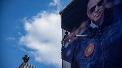 Полицейский с биноклем на крыше здания рядом с гигантским баннером с изображением президента Турции Реджепа Тайипа Эрдогана во время предвыборного митинга (13 мая 2023). Стамбул