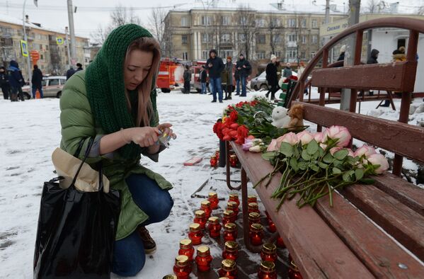 Женщина зажигает свечу возле здания торгового центра Зимняя вишня в Кемерово, где произошел пожар - Sputnik Армения