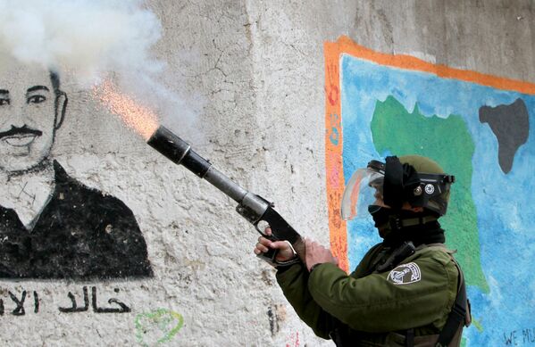 Израильский пограничник стреляет баллоном со слезоточивым газом в сторону палестинских протестующих во время столкновений после пятничной молитвы в лагере беженцев Аида, недалеко от города Вифлеем, 13 февраля 2015 года - Sputnik Армения