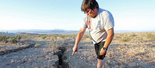 Мужчина показывает расщелину, которая открылась в пустыне после мощного землетрясения недалеко от города Риджкрест (4 июля 2019). Калифорния - Sputnik Армения