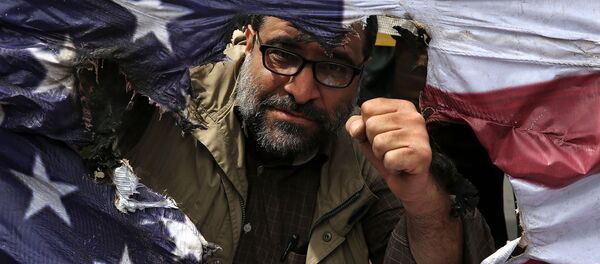 Иранский протестующий сжимает кулак за сожженным изображением флага США во время собрания после пятничной молитвы (11 мая 2018). Тегеран - Sputnik Армения