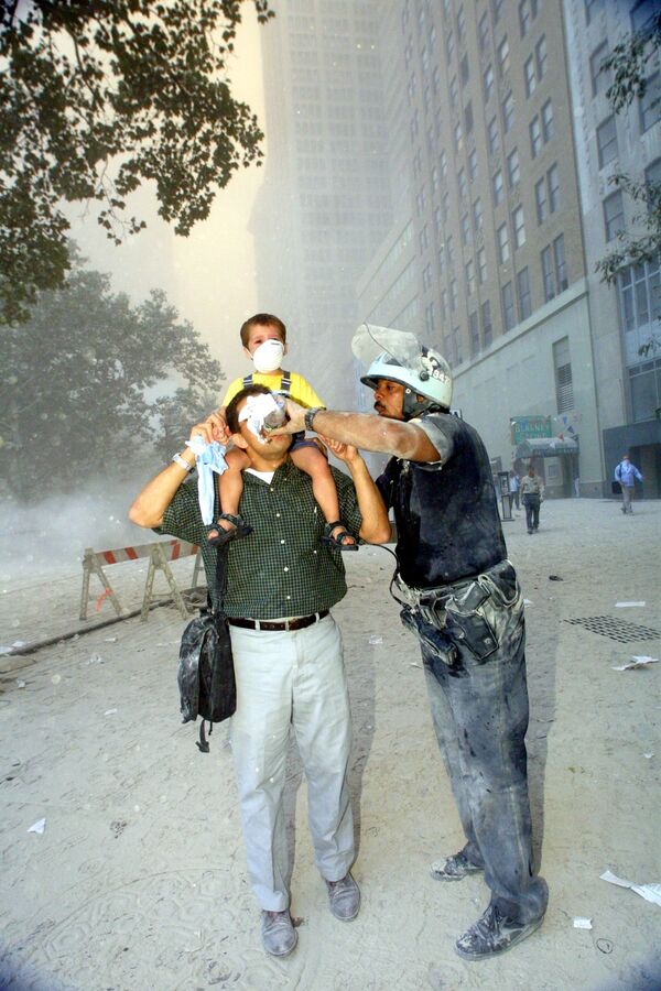 Полицейский помогает при эвакуации людей из Всемирного торгового центра 11 сентября 2001 года - Sputnik Армения