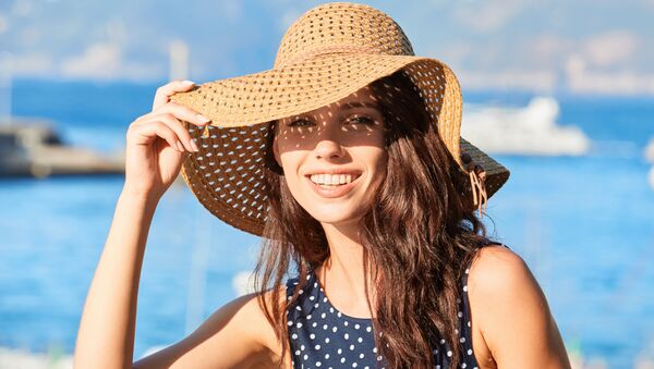 Красивая молодая женщина в летней шляпе прикрывает глаза от солнца и улыбается  - Sputnik Армения