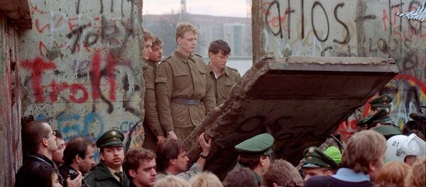 Восточногерманские пограничники видны через щель в Берлинской стене после того, как демонстранты снесли сегмент стены у Бранденбургских ворот (11 ноябрq 1989). Берлин - Sputnik Արմենիա