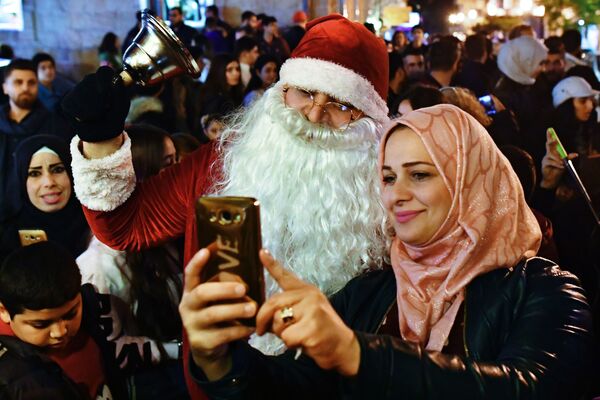 Женщина фотографируется с мужчиной в костюме Санта-Клауса на праздновании Рождества в сирийской Латакии - Sputnik Армения