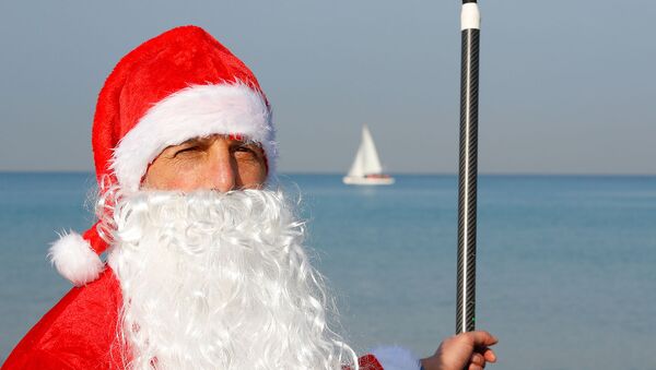 Израильский спасатель Арут Торосян в костюме Санта-Клауса позирует с веслом и доской на пляже (22 декабря 2019). Тель-Авив - Sputnik Արմենիա
