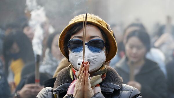 Женщина в маске и солнцезащитных очках во время молитвы в первый день Нового года в Пекине - Sputnik Արմենիա