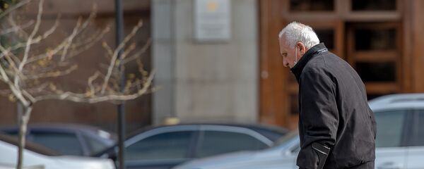 Пожилой человек в защитной маске проходит мимо правительственного здания (30 марта 2020). Еревaн - Sputnik Армения