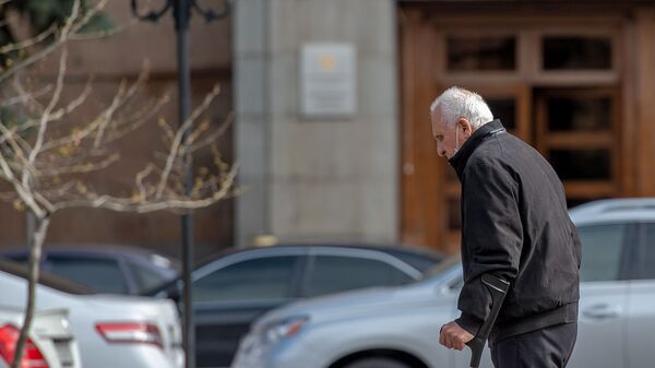 Пожилой человек в защитной маске проходит мимо правительственного здания (30 марта 2020). Еревaн - Sputnik Армения