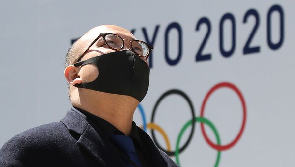 Мужчина в защитной маске проходит перед логотипом токийской Олимпиады (25 марта 2020). Токио - Sputnik Армения