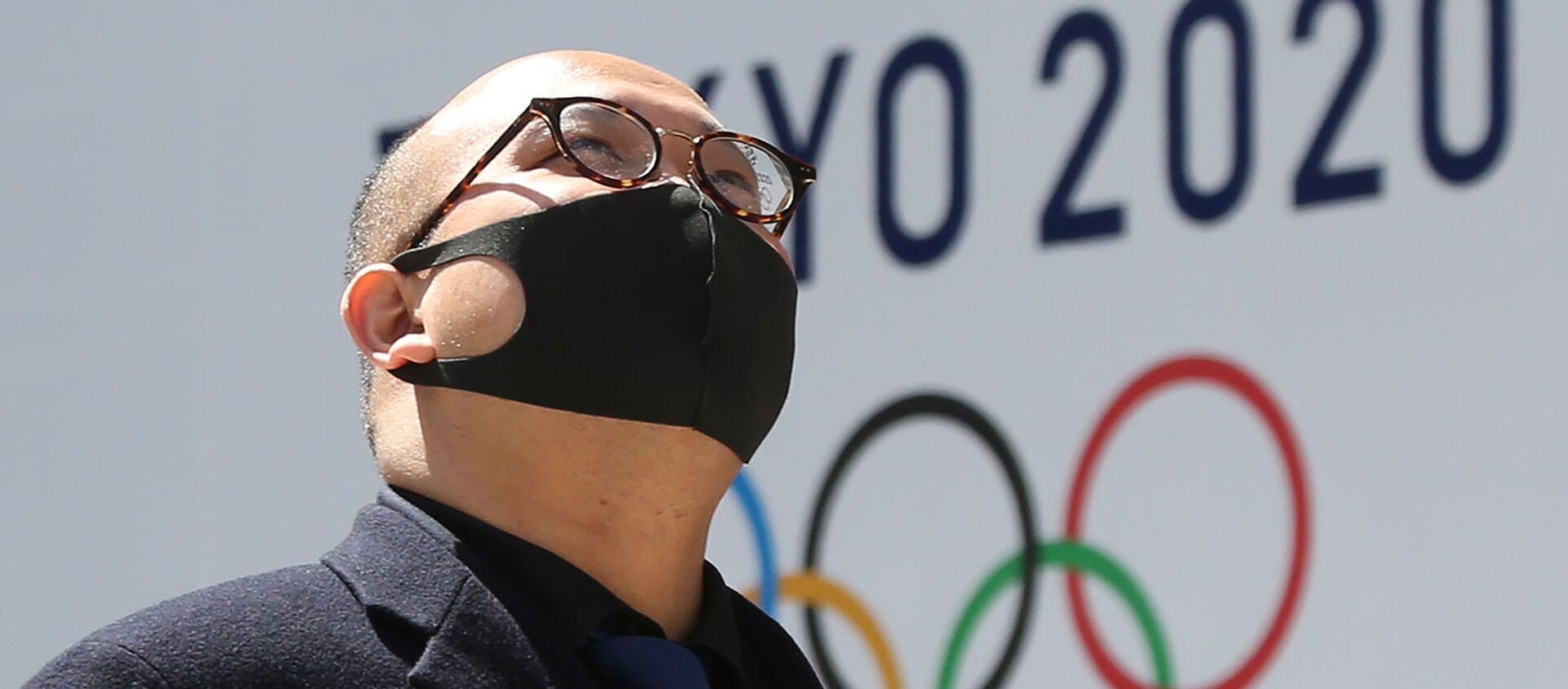 Мужчина в защитной маске проходит перед логотипом токийской Олимпиады (25 марта 2020). Токио - Sputnik Արմենիա, 1920, 31.07.2021
