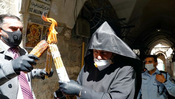 Армянский священник в защитной маске и перчатках передает Благодатный огонь, зажженный в храме Гроба Господня (18 апреля 2020). Иерусалим - Sputnik Армения