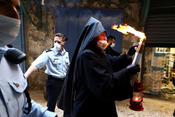 Армянский священник в защитной маске и перчатках держит Благодатный огонь, зажженный в храме Гроба Господня (18 апреля 2020). Иерусалим - Sputnik Армения