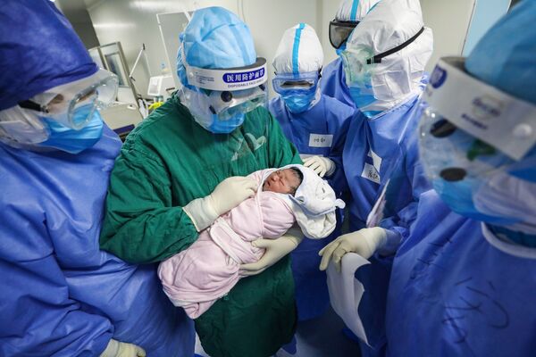 Медицинский работник в защитном костюме держит на руках новорожденного в отделении для инфицированных коронавирусом беременных в больнице Уханя, Китай - Sputnik Армения