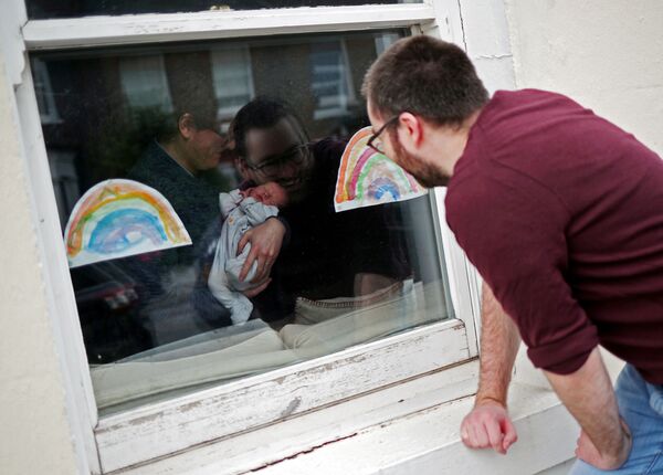 Мужчина смотрит через окно на свою новорожденную племянницу в период пандемии коронавируса в Великобритании - Sputnik Армения