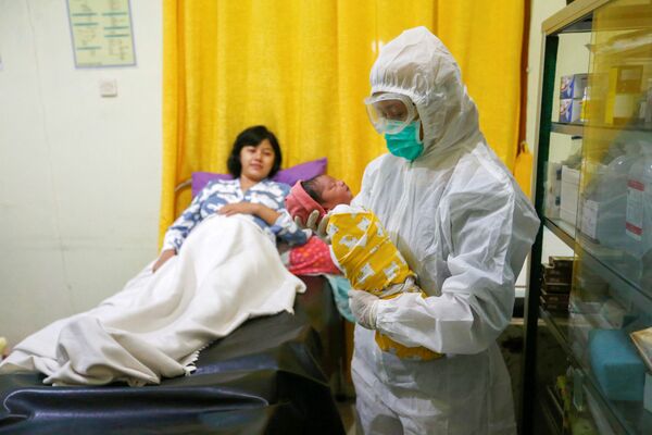 Медсестра в защитном костюме держит новорожденного в родильном отделении в Депоке, недалеко от Джакарты, Индонезия - Sputnik Армения