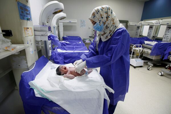 Медсестра в защитной маске и перчатках ухаживает за новорожденным в роддоме в Наджафе, Ирак - Sputnik Армения