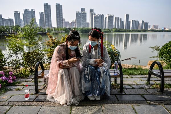 Молодые женщины в масках и в традиционных костюмах на скамейке в парке Уханя, Китай - Sputnik Армения